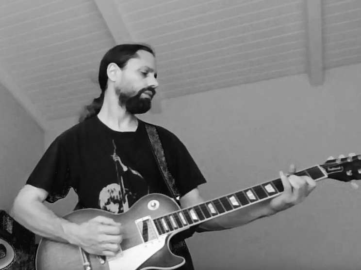 musician wearing a black tom petty t-shirt playing an electric guitar in a room with plain walls