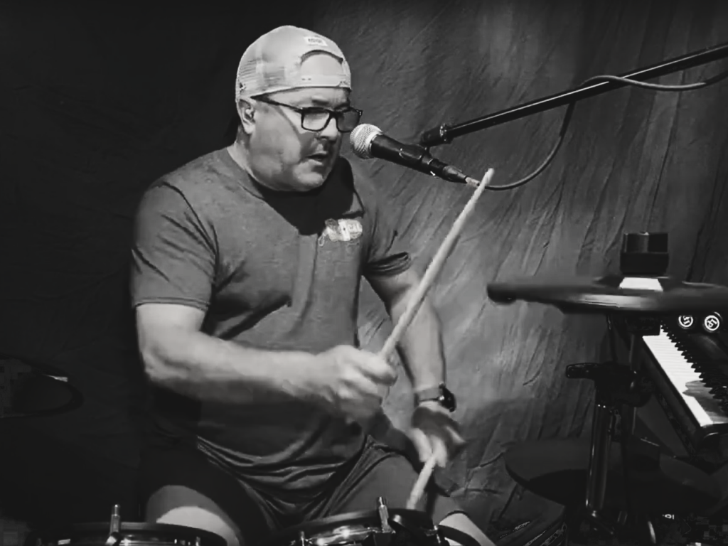 musician playing the drums with a canvas-type backdrop behind him