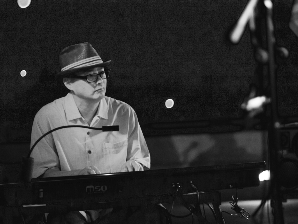 musician in a stylish hat playing the keyboards with small lights shining behind him